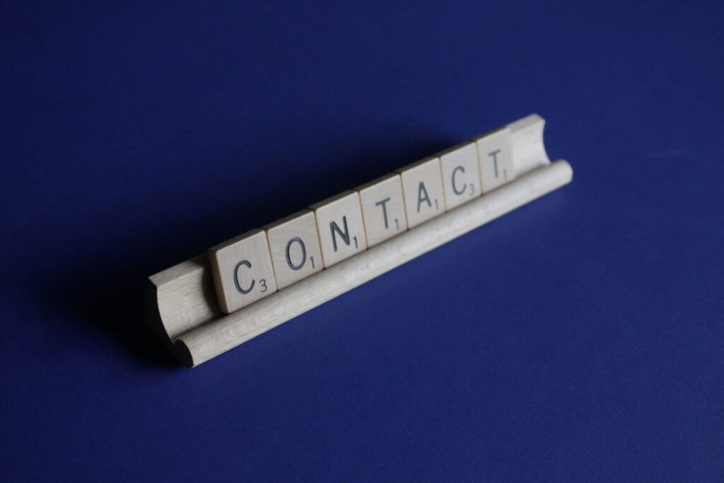 Wooden letter tiles spelling 'Contact' on a blue background for German to English translator's contact page