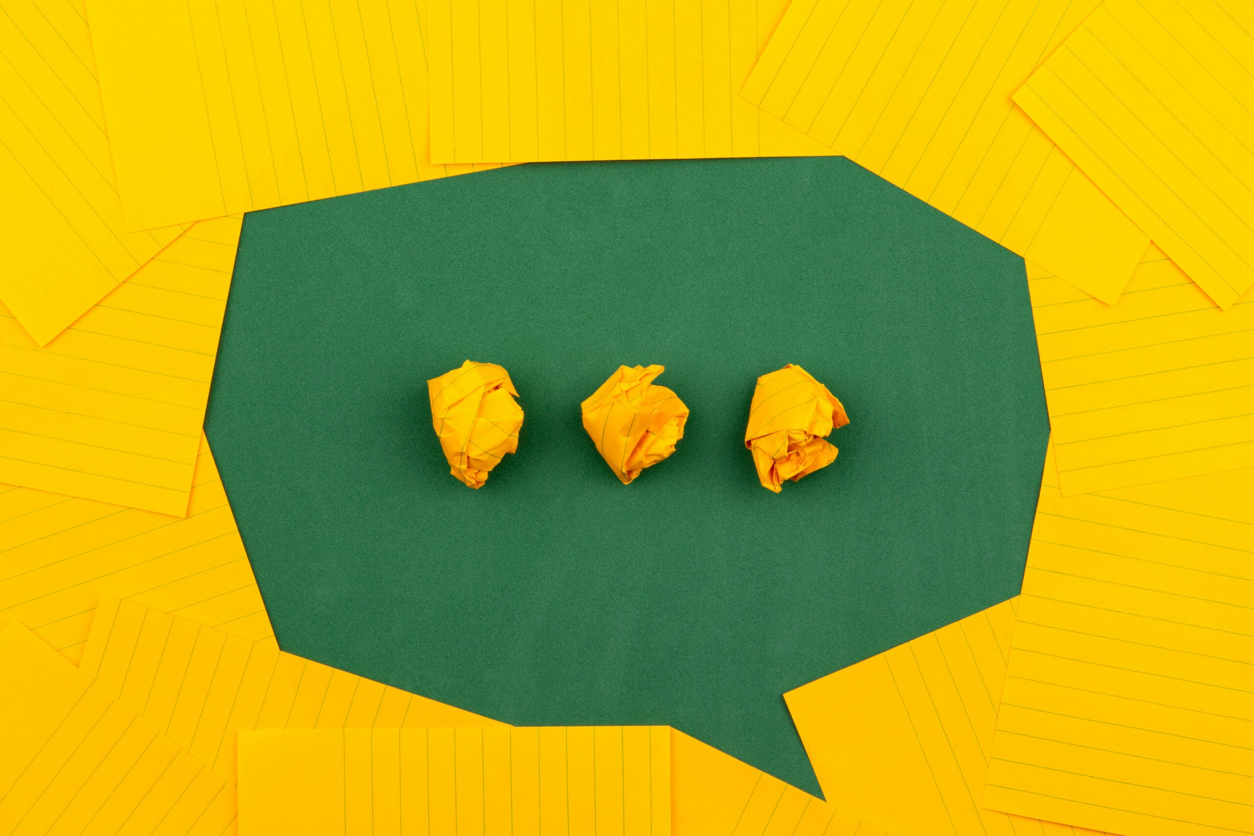 Green speech bubble made of yellow note cards with crumpled paper inside, symbolising communication and creative challenges