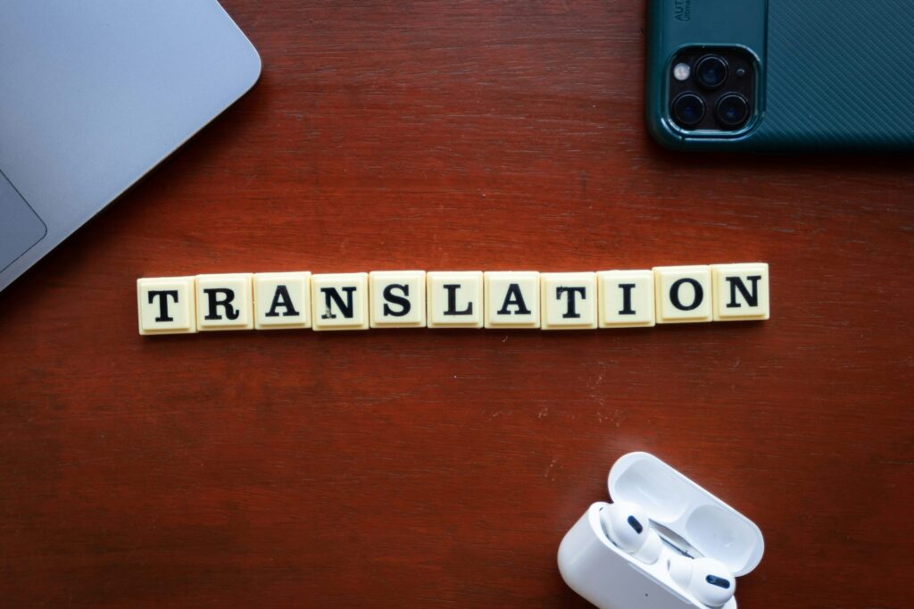 The word 'Translation' spelled out in Scrabble-style tiles with a laptop, smartphone, and earbuds nearby