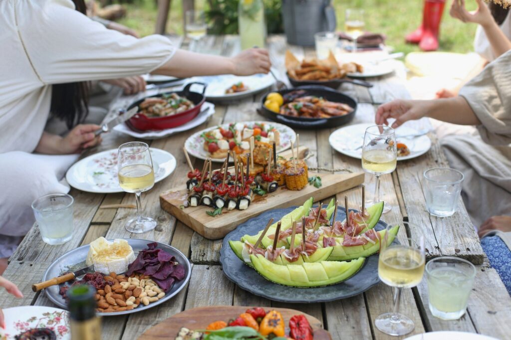 Shared outdoor meal with assorted small dishes, wine, and people dining together